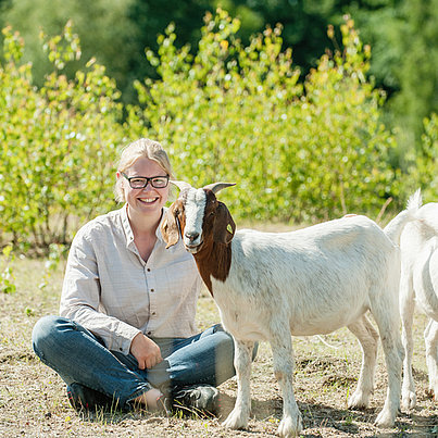 Junge Frau mit Ziege im Gras im FSJ Bauernhof