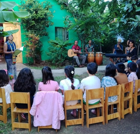 Waldorf Oceania Rapa Nui Children sit outside on chairs and listen to a storyteller and a music group.